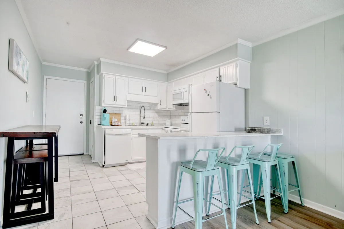 A bright, open kitchen space featuring a kitchen island with bar stools, white cabinetry, and modern appliances. The setting suggests a peaceful place to prepare or enjoy breakfast, with lots of natural light and a casual, welcoming atmosphere ideal for couples sharing a quiet meal.