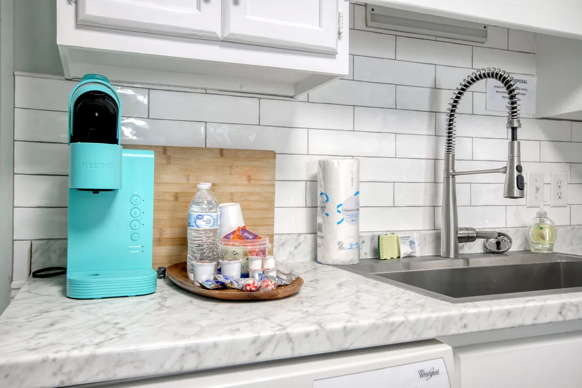 Focuses on a turquoise coffee maker, wooden cutting board, a tray of condiments, and the kitchen sink. The setup suggests morning routines, food prep, and a cozy, functional kitchen ready for family activity.