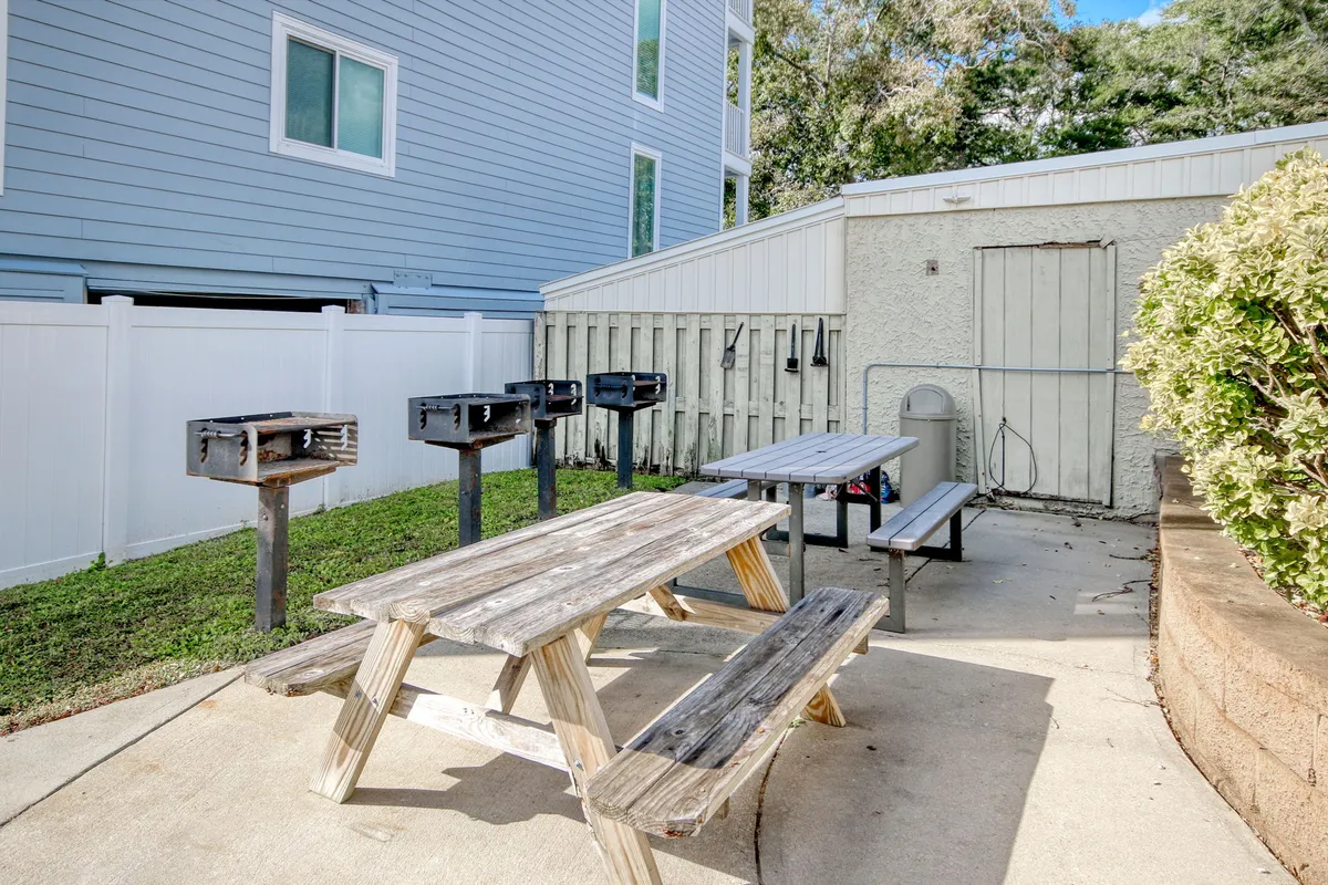 A relaxed exterior setting featuring a picnic table and barbecue grills, surrounded by greenery with the building's exterior visible. The space is ideal for outdoor grilling, picnics, and casual socializing, making it perfect for family barbecues or group celebrations after a day by the sea.
