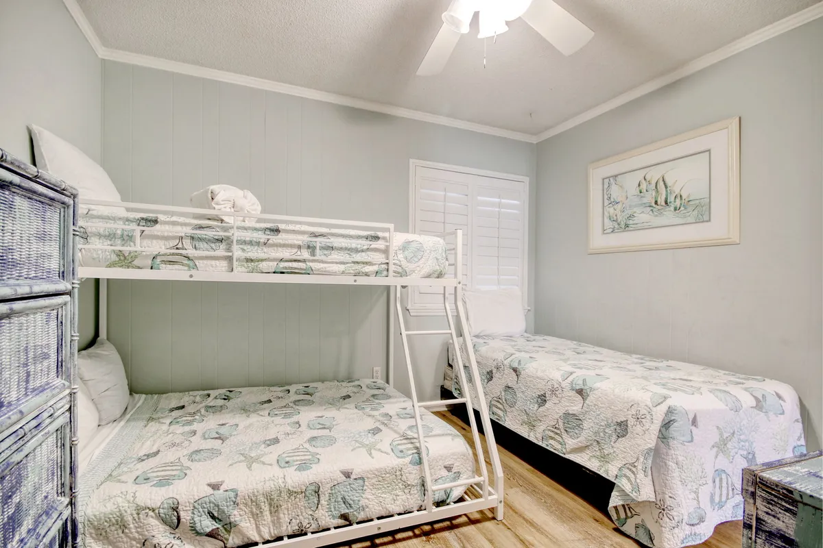 A playful bedroom setup featuring a bunk bed and a single bed, accented by decorative artwork and woven furniture. The room exudes a relaxed, family-friendly vibe perfect for children or groups of friends.