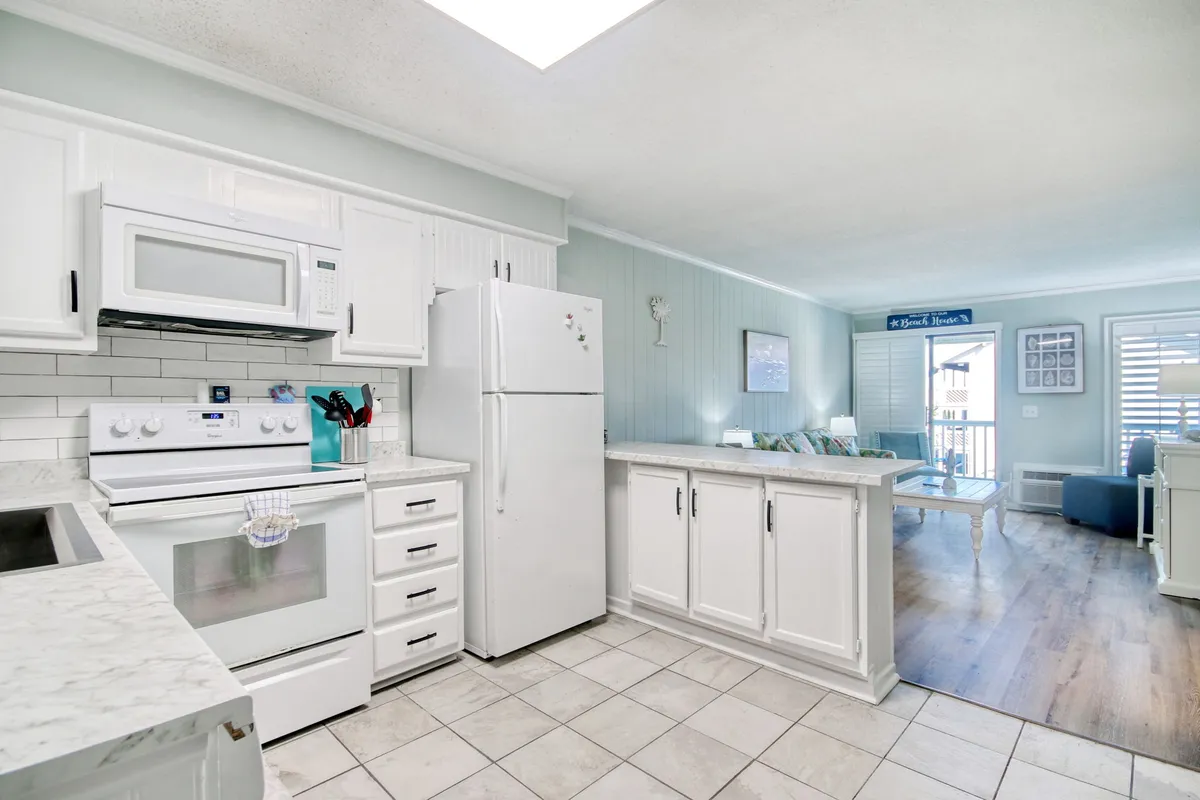 A bright, open kitchen with modern appliances, gleaming marble countertops, and white cabinetry, seamlessly connected to the living area. The space is designed for gathering, preparing drinks, or sharing meals with friends before heading out for the night.