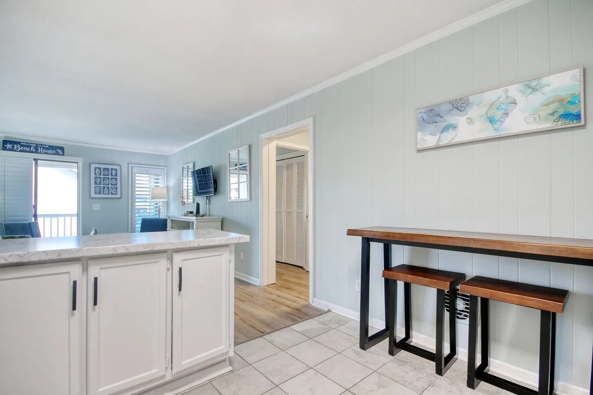 A view of the kitchen island with wooden bar stools and a decorative art piece on the wall. The island invites casual dining and socializing, offering a relaxed and functional setting for breakfast or late-night snacks.